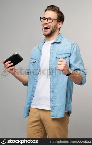 Young handcome man playing with portable video game standing over grey background.. Young handcome man playing with portable video game standing over grey background