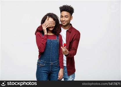 Young handsome African American closing her girlfriend eye and surprising proposal with ring.. Young handsome African American closing her girlfriend eye and surprising proposal with ring