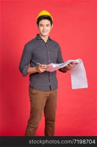 Young handsome asian man in casual dress with yellow hardhat hand holding paperwork blueprint in architect and engineer worker isolated in red background in studio.
