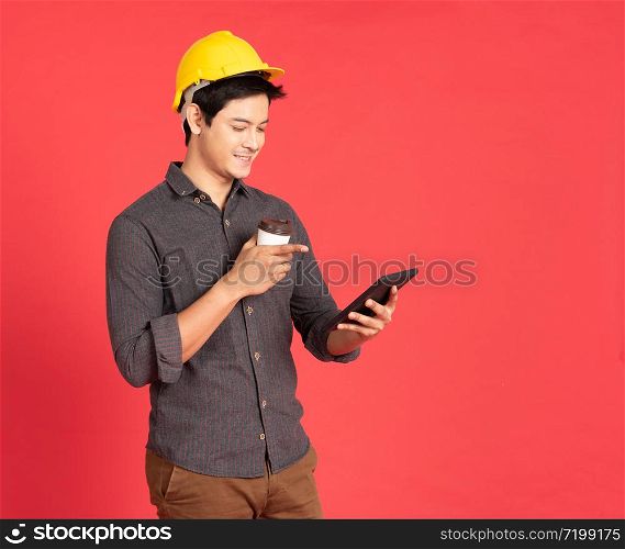 Young handsome asian man in casual dress with yellow hardhat hand holding laptop in architect and engineer worker isolated in red background in studio.