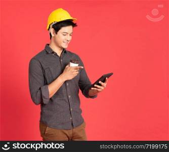 Young handsome asian man in casual dress with yellow hardhat hand holding laptop in architect and engineer worker isolated in red background in studio.
