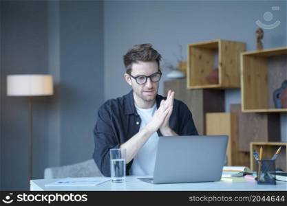 Young handsome austrian male freelancer wearing glasses looking at computer screen attentively, checking important e-mail on laptop or reading internet media while working remotely at home. Young handsome austrian male freelancer wearing glasses looking at computer screen attentively