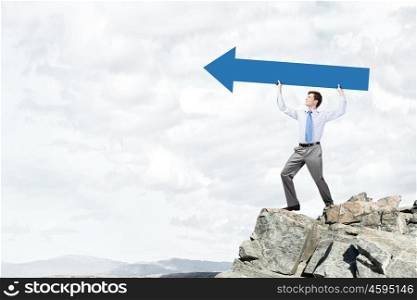 Young handsome businessman holding in hands huge arrow . Businessman showing direction