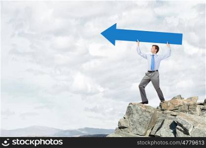 Young handsome businessman holding in hands huge arrow . Businessman showing direction