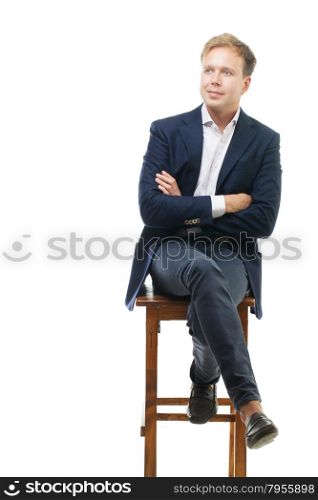 Young handsome businessman sitting on high wooden chair with crossed arms. He staring in the distance with slight smile. Confident and reliable person. Isolation white background