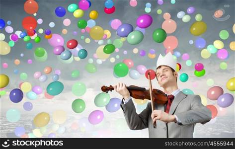 Young handsome businessman wearing white paper crown and playing violin