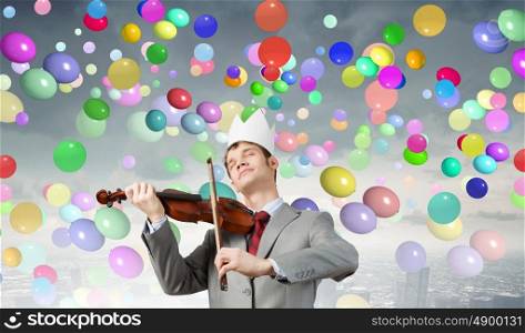 Young handsome businessman wearing white paper crown and playing violin