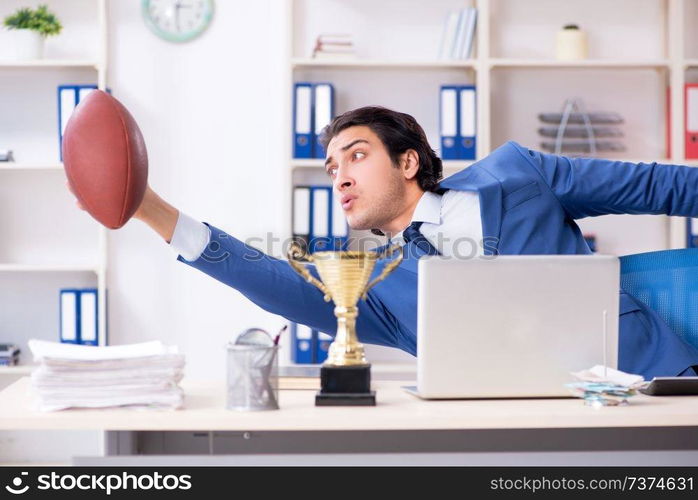 Young handsome businessman with rugby ball in the office