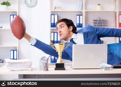 Young handsome businessman with rugby ball in the office