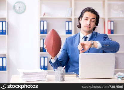 Young handsome businessman with rugby ball in the office