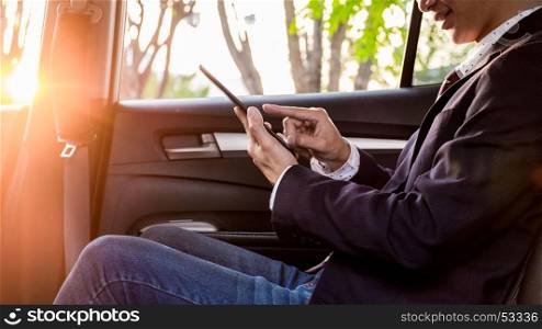 young handsome businessman working in back of car and using a tablet or smart phone.
