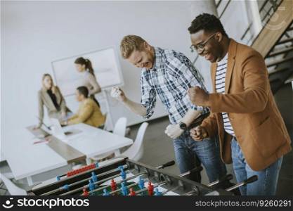 Young handsome casual multiethnic business people playing table football and relaxing at office