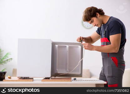 Young handsome contractor repairing fridge . Young handsome contractor repairing fridge
