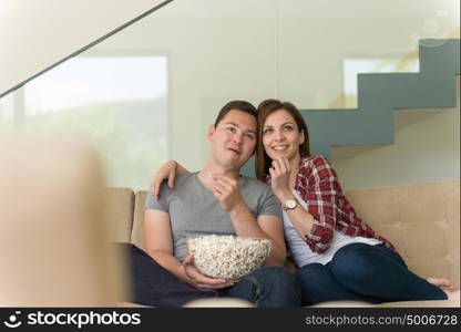 young handsome couple enjoying free time watching television with popcorn in their luxury home villa