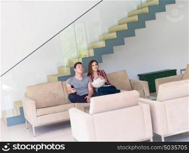 young handsome couple enjoying free time watching television with popcorn in their luxury home villa