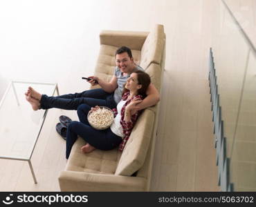 young handsome couple enjoying free time watching television with popcorn in their luxury home villa