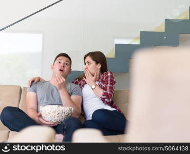 young handsome couple enjoying free time watching television with popcorn in their luxury home villa