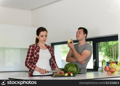 Young handsome couple in the kitchen beautiful woman preparing a salad while the man eating an apple