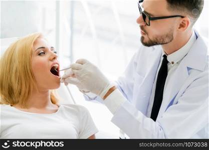 Young handsome dentist examining teeth of happy woman patient sitting on dentist chair in dental clinic. Dentistry care concept.