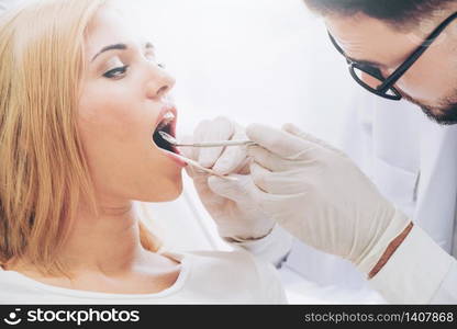 Young handsome dentist examining teeth of happy woman patient sitting on dentist chair in dental clinic. Dentistry care concept.. Young dentist examining patient in dental clinic.