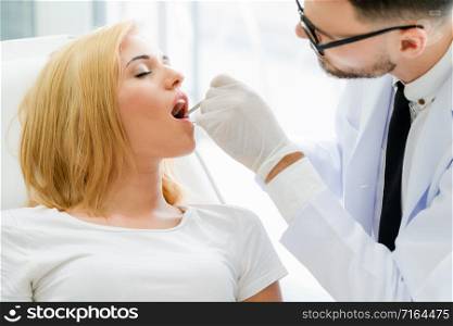 Young handsome dentist examining teeth of happy woman patient sitting on dentist chair in dental clinic. Dentistry care concept.. Young dentist examining patient in dental clinic.