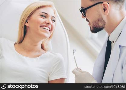 Young handsome dentist talks with happy woman patient sitting on dentist chair in dental clinic. Dentistry care concept.