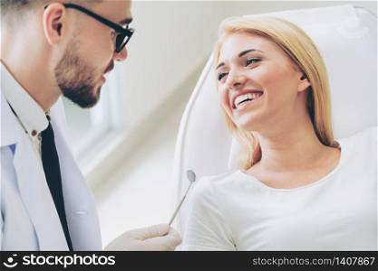 Young handsome dentist talks with happy woman patient sitting on dentist chair in dental clinic. Dentistry care concept.. Young dentist talks with patient in dental clinic.