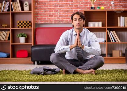 Young handsome employee doing yoga in the office 
