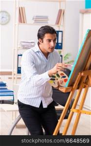 Young handsome employee enjoying painting at the office 