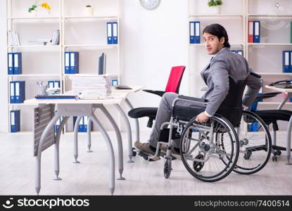 Young handsome employee in wheelchair working in the office  