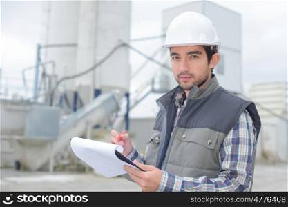 young handsome foreman writing on his clipboard at construction site