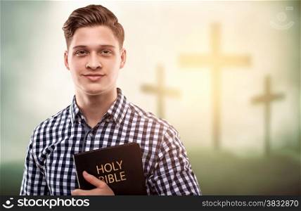 Young handsome happy man holding a Bible with tree crosses background (easter concept)