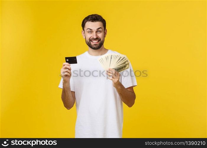 Young handsome happy smiling man holding banking card and cash in his hands isolated on yellow background. Young handsome happy smiling man holding banking card and cash in his hands isolated on yellow background.