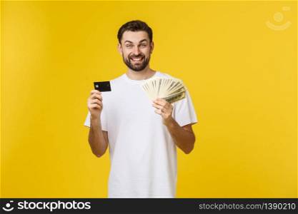 Young handsome happy smiling man holding banking card and cash in his hands isolated on yellow background. Young handsome happy smiling man holding banking card and cash in his hands isolated on yellow background.