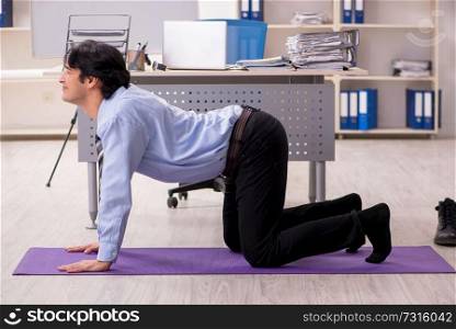Young handsome male employee doing exercises in the office 
