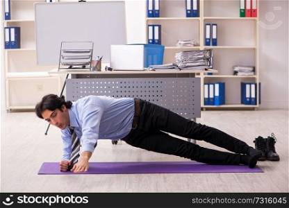 Young handsome male employee doing exercises in the office 