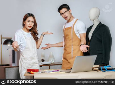 Young handsome man and pretty woman, Couple designer has conflict together while use laptop computer chatting with customer online order, mannequin and tailoring tools on desk