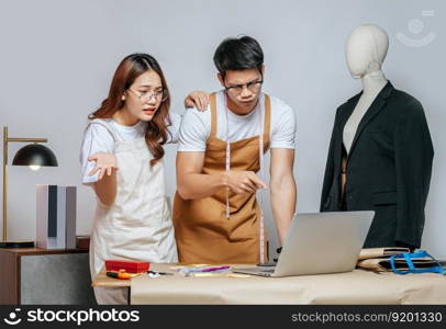 Young handsome man and pretty woman, Couple designer has conflict together while use laptop computer chatting with customer online order, mannequin and tailoring tools on desk