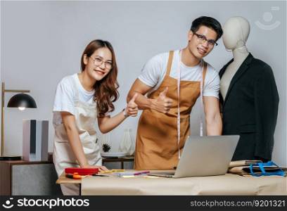 Young handsome man and pretty woman, Couple designer use laptop computer for searching good idea to design fashion clothing and chatting to customer online order, mannequin and tailoring tools on desk
