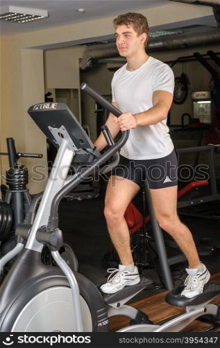 young handsome man does workout at elliptical trainer in gym