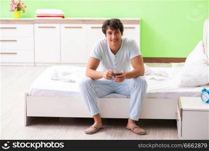 Young handsome man drinking coffee in the bed 