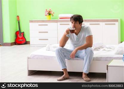 Young handsome man drinking coffee in the bed 