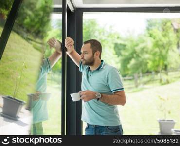 young handsome man drinking morning coffee by the window in his home