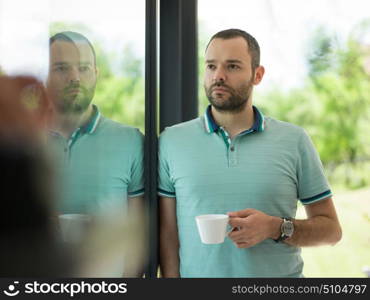 young handsome man drinking morning coffee by the window in his home