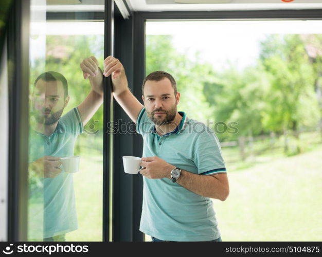 young handsome man drinking morning coffee by the window in his home