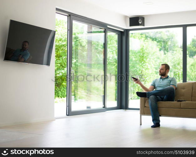 young handsome man enjoying free time watching television in his luxury home villa