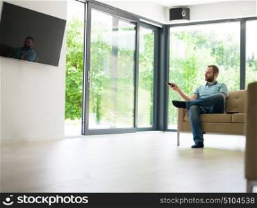 young handsome man enjoying free time watching television in his luxury home villa
