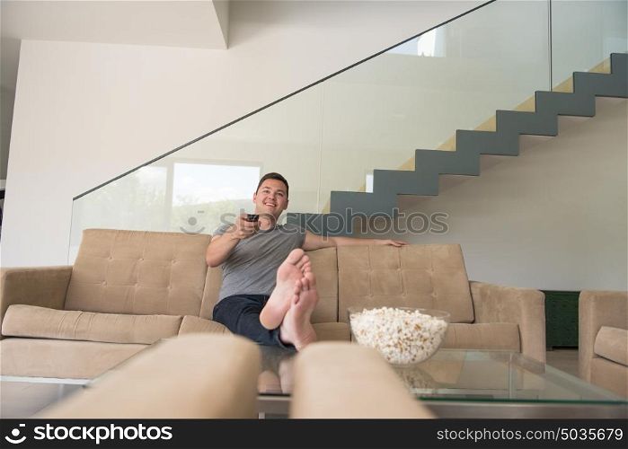 young handsome man enjoying free time watching television with popcorn in his luxury home villa