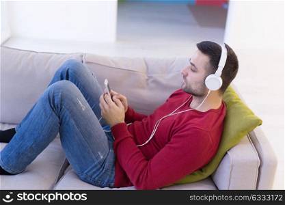 Young handsome man enjoying music through headphones, laying on sofa at home