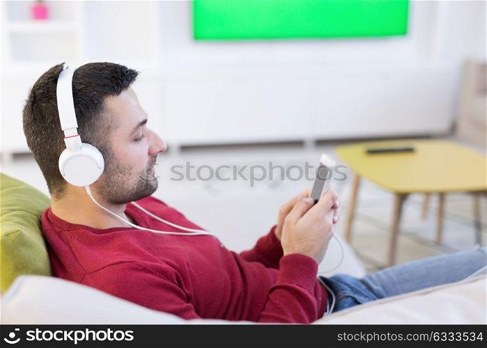 Young handsome man enjoying music through headphones, laying on sofa at home